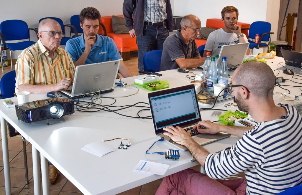 A group of older male participants and researchers working on laptop computers together, exploring Arduino.