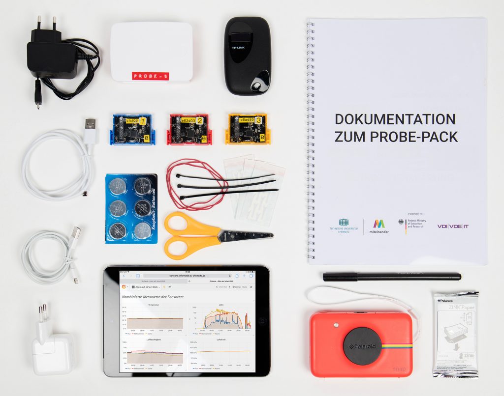 Sensing Home Probe Pack laid flat on a table, consisting of three texas instruments SensorTags, one iPad, one instant camera and film, a documentation, one wifi router, one rapsberry pi and material to attach the sensor tags onto everyday things