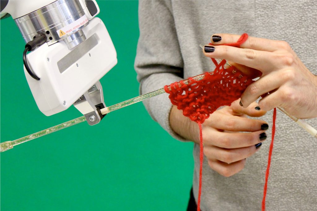 Robot arm on the left holds a needle in order for the human on the knit with them